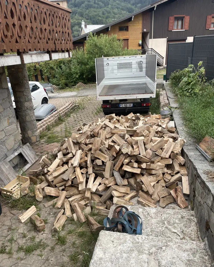 Tas de bûches livrées devant un chalet, camion-benne en arrière-plan